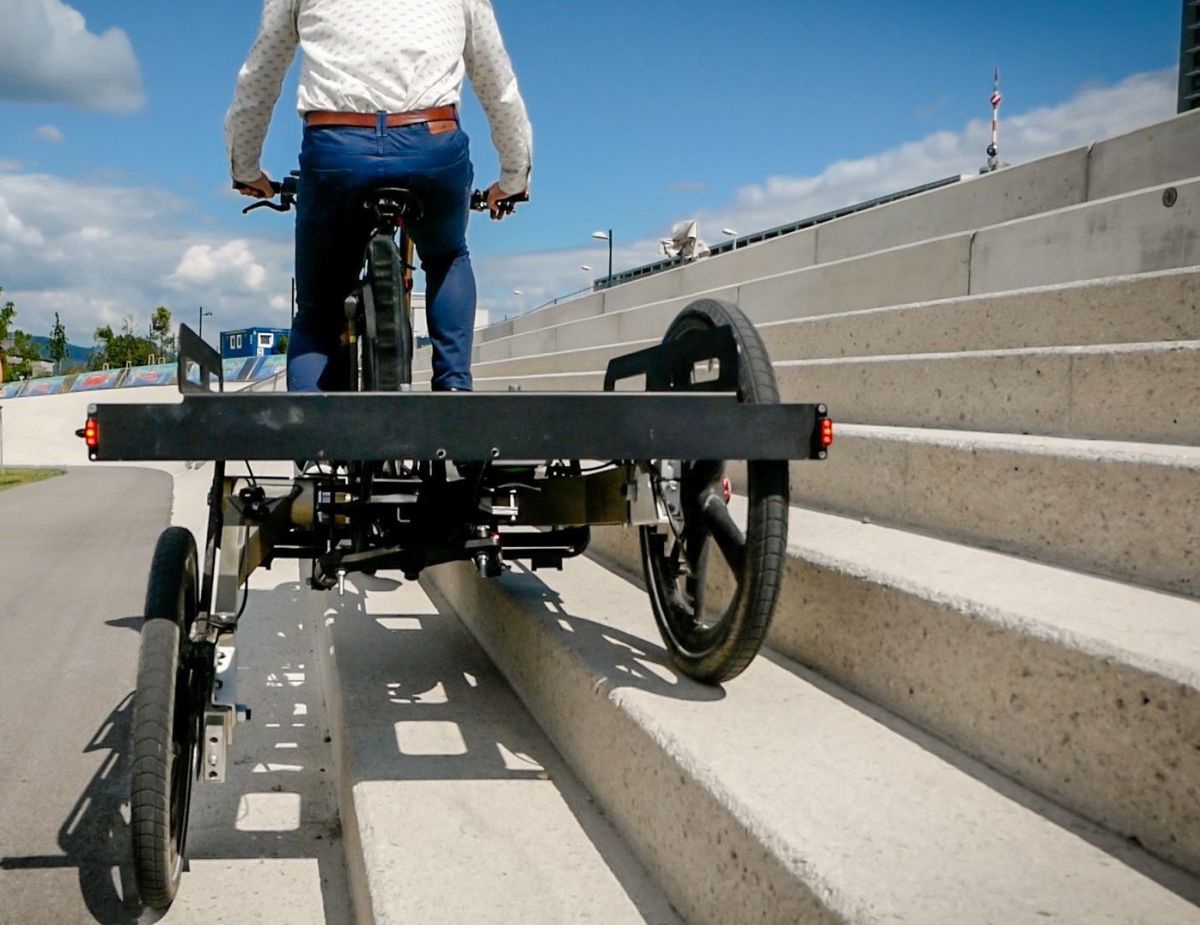 Ansicht von hinten. Das Fahrrad steht auf einer Treppe, mit einem Hinterreifen zwei Stufen unter dem anderen Hinterreifen. Die Ladefläche ist dabei immer noch gerade.