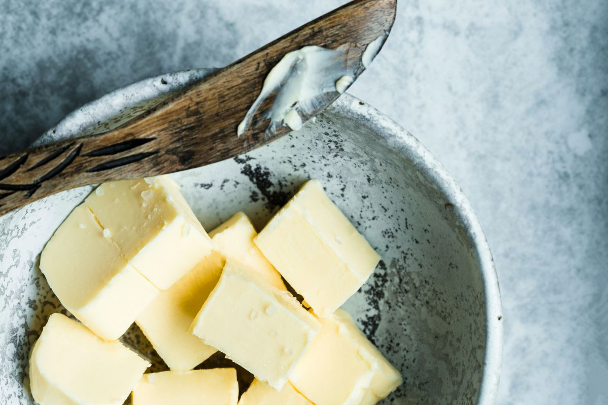 Eine Schüssel mit Butterwürfeln, darauf liegt ein Buttermesser aus Holz.