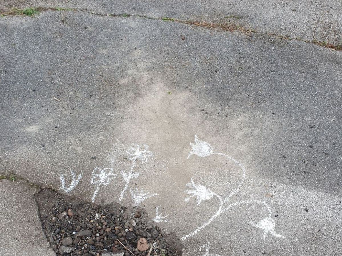 Um ein mit Schotter und Asphaltbrocken gefülltes Loch im Straßenbelag hat jemand mit weißer Kreide Blumen gezeichnet.