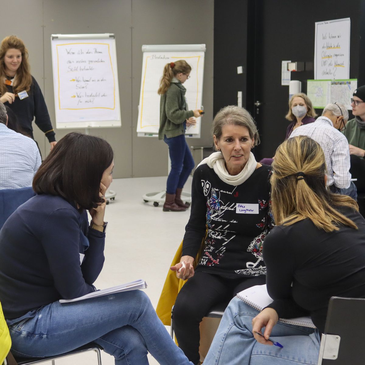 Der Zukunftsrat Verkehr bei der Arbeit: Menschen sitzen zusammen in kleineren Gruppen in einem Seminarraum und sind ins Gespräch vertieft. Einige notieren Ideen auf den bereitgestellten Flip-Charts.