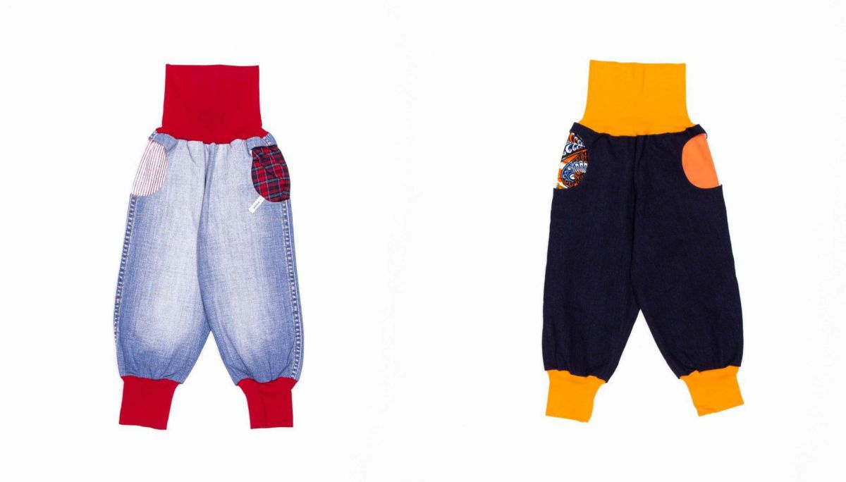 Zwei bunte Kinderhosen mit weitem Bein, runden Taschen und breiten, elastischen Bünden an Bauch und Knöcheln. Die Hose links im Bild ist aus upgecycelten Bluejeans genäht, mit roten Bünden. Die Hose rechts aus dunkelblauem Jeansstoff mit gelben Bünden.