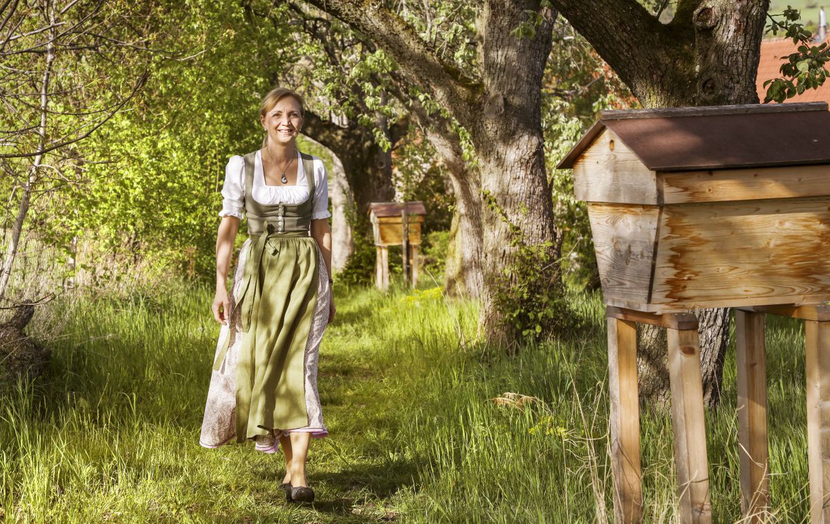 Eine Frau in Tracht spaziert auf einer Wiese auf die Kamera zu.