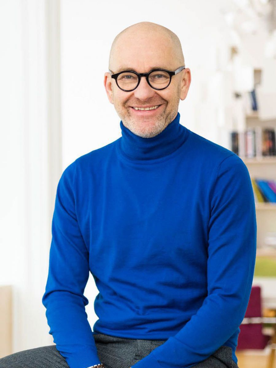 Mann mit Brille sitzt auf einem Stuhl in seinem Büro und lächelt in die Kamera. 