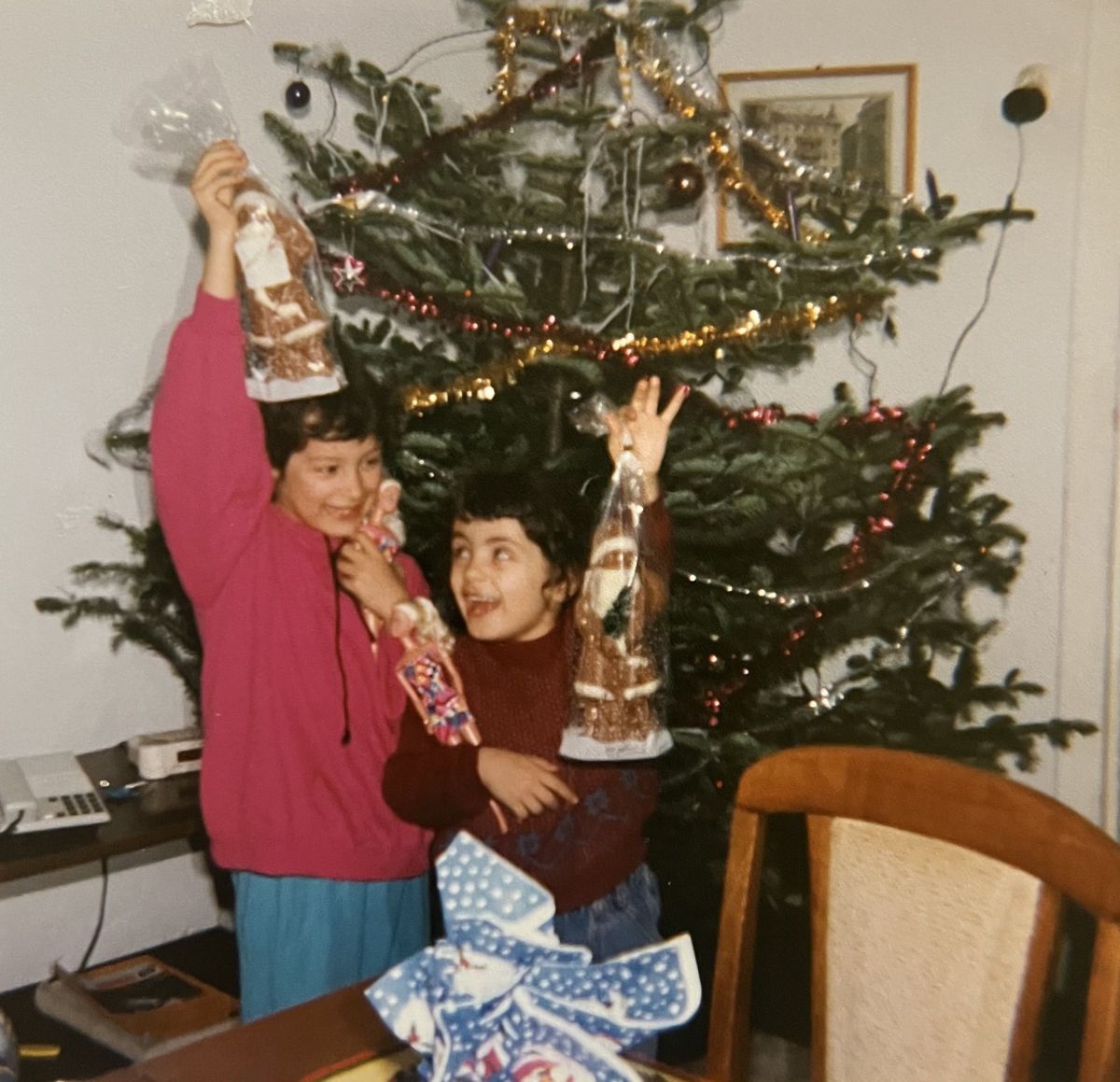 Zwei Mädchen präsentieren stolz ihre Weihnachtsgeschenke vor dem geschmückten Christbaum.